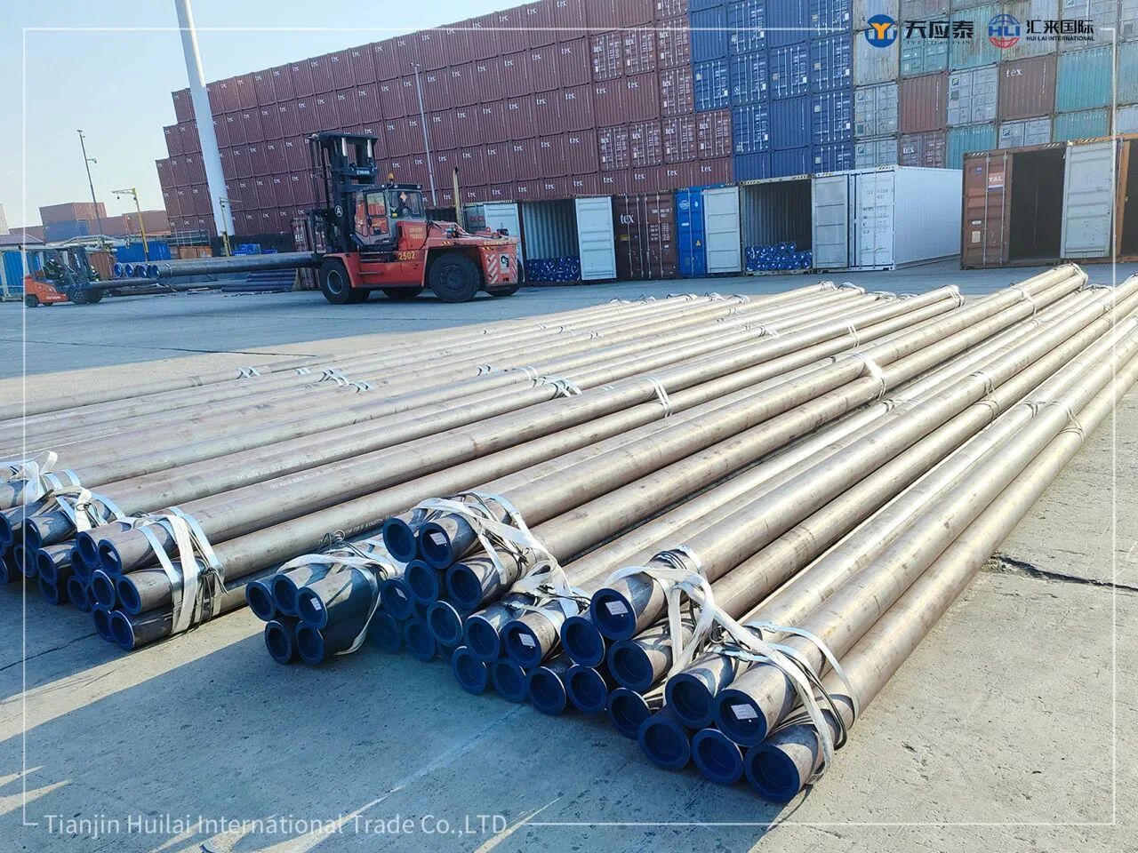 Bundled seamless steel pipes staged beside shipping containers
